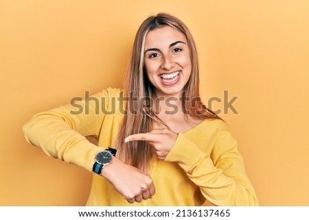 Beautiful hispanic woman wearing casual yellow sweater in hurry pointing to watch time, impatience, upset and angry for deadline delay 