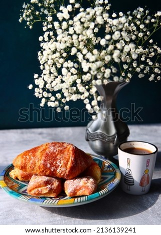 Good morning! Black coffee and croissants on a table. Sunny picture with pastries and flowers. Food still life photo. 