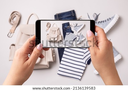 Woman taking photo of clothes (jeans, t-shirt, sneakers, backpack) with smartphone. Blogger, influencer or stylist capturing spring fashion outfit and accessories for social media. Royalty-Free Stock Photo #2136139583