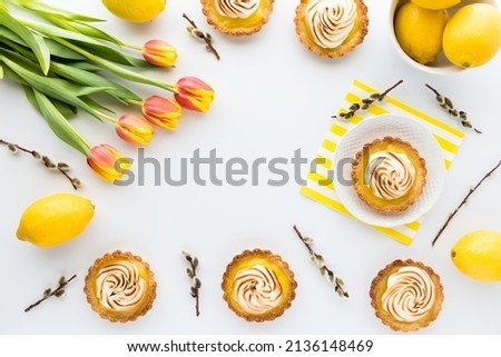 Homemade lemon meringue tartlets surrounded by pussy willows and tulips.