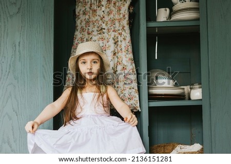 little cute Armenian girl sit in retro vintage wardrobe and playing hide-and-seek in country house and having fun, concept of simple life and spring