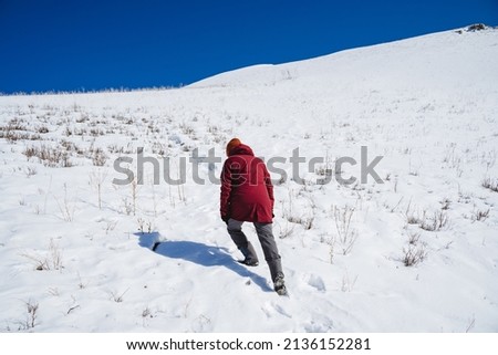 A man in a red jacket climbs uphill on foot. The climber climbs to the top of the mountain in the snow. High quality photo