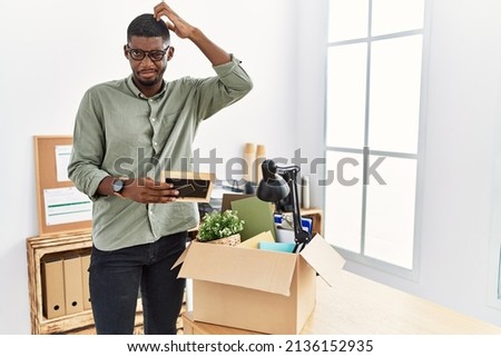 Young african american businessman unboxing box at the office confuse and wondering about question. uncertain with doubt, thinking with hand on head. pensive concept. 