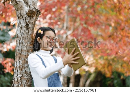 Happy smiling cute little girl with glasses holding book over nature background. 