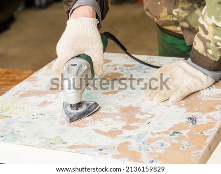 a man using a grinder removes old paint from furniture, restoration of antique furniture. handmade concept Royalty-Free Stock Photo #2136159829