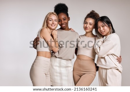 beauty portrait of diverse women, caucasian, asian and african american ladies with different skintone posing at camera, hugging each other, dressed casually in beige tone clothes. isolated Royalty-Free Stock Photo #2136160241