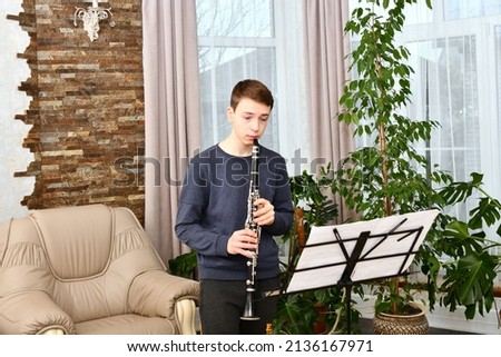 A young guy plays the clarinet from notes. Learning music at home.