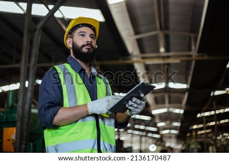 Portrait of man engineer wear yellow helmet holding tablet and uniform standing at industrial workshop. handsome workman with beard on face in factory. Copy space. Royalty-Free Stock Photo #2136170487