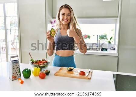 Young caucasian fitness woman wearing sportswear preparing healthy salad at the kitchen smiling happy and positive, thumb up doing excellent and approval sign 