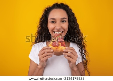 Closeup Portrait Of Excited Young Lady Enjoying Pizza Holding And Biting Tasty Slice Standing Over Yellow Orange Studio Background. Junk Food Lover Eating Italian Pizza. Unhealthy Nutrition Cheat Meal Royalty-Free Stock Photo #2136178825