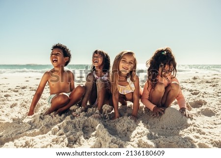 Four young friends laughing cheerfully while playing with sea sand at the beach. Group of adorable little kids having a good time together during summer vacation. Royalty-Free Stock Photo #2136180609