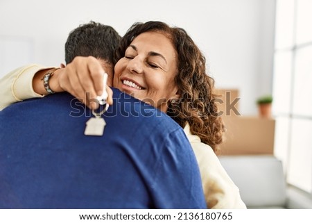 Middle age hispanic couple smiling happy and hugging. Standing with smile on face holding key of new home. Royalty-Free Stock Photo #2136180765