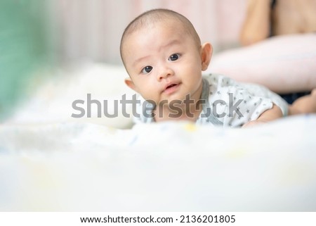 Happy family, Cute Asian newborn baby lying play on bed looking at something. While your mother takes care with love nearby. Innocent little boy on the first day of his life. Mother's Day concept.