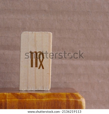 Close-up shot of a piece of wood with a zodiac sign engraved on it, especially the virgo sign