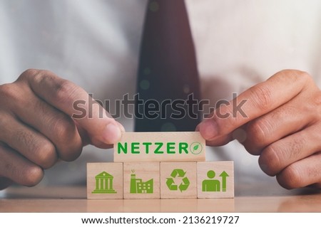Hand puts wooden cubes with net zero icon in Net zero on grey background. Net zero by 2050. Carbon neutral. Net zero greenhouse gas emissions target. Climate neutral long term strategy. Royalty-Free Stock Photo #2136219727
