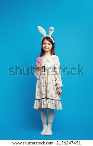Full length body size photo of pretty cheerful child holding in hands tasty cookie in shape of heart, isolated on blue color background