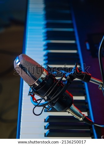 Studio microphone on the background of a piano keyboard. The concept of vocal, blogger and sound recording. Background for karaoke and recording studio, colored light
