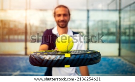 Monitor of padel holding black racket with yellow tennis ball over. Class to student on outdoor tennis court. Man paddel player playing a match in the open Royalty-Free Stock Photo #2136254621