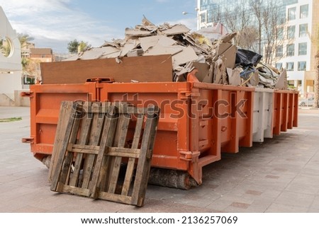 huge heap on metal Big  Overloaded dumpster waste container filled with construction waste, drywall and other rubble near a construction site. Royalty-Free Stock Photo #2136257069