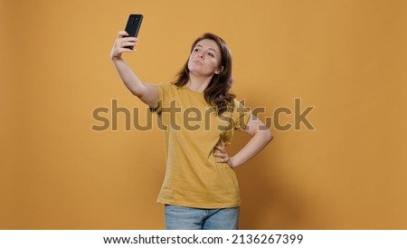 Portrait of woman using smartphone to take a selfie feeling confident and beautiful striking multiple poses in studio. Person using mobile phone taking picture using camera to post on social media.