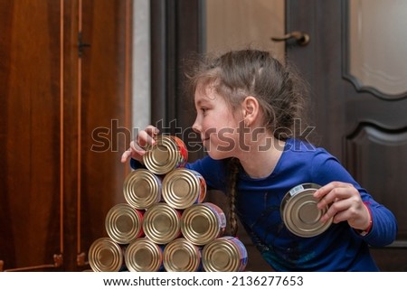 The child is playing with jars of canned fish. The girl is playing with a supply of food.