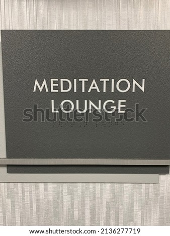 A rectangular sign that has the word "MEDITATION ROOM" engraved into it. The sign is grey and is attached to the wall.