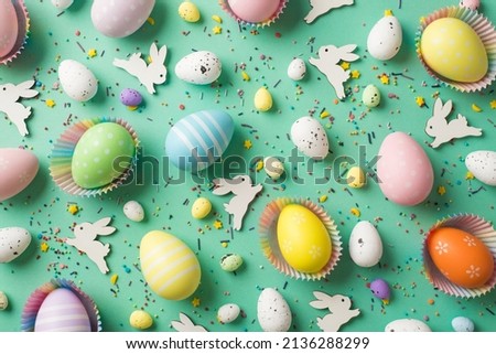 Top view photo of easter decorations multicolored easter eggs in paper baking molds confectionery topping and easter bunnies on isolated pastel green background