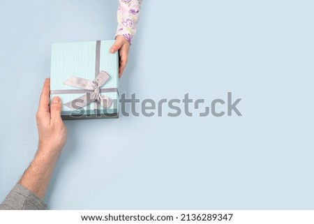 a father receives a gift box with a bow from the hands of his child in close-up