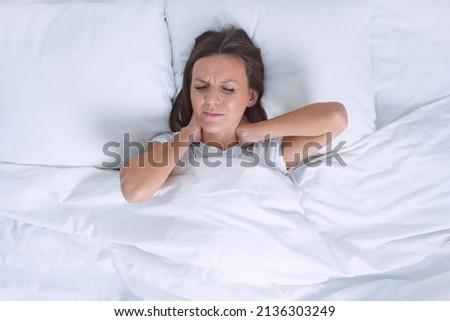 Woman in bed suffering from neck pain in the morning after sleeping on uncomfortable pillow. Pain in neck, cervical chondrosis or osteochondrosis Royalty-Free Stock Photo #2136303249