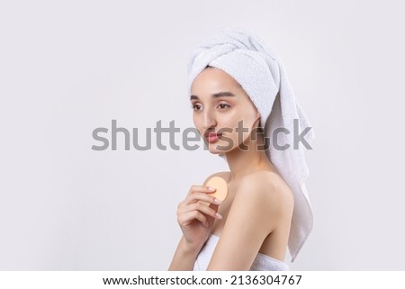 Beautiful girl with thick eyebrows and perfect skin at white background, towel on head, beauty photo. Holds a cosmetic sponge.