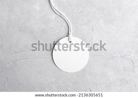 Round white tag mockup with white cord, close up. Blank paper price tag isolated on grey stone background with copy space.