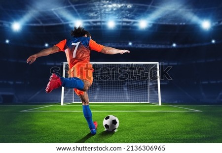 Soccer scene at night match with player in an orange and blue uniform kicking the penalty kick Royalty-Free Stock Photo #2136306965