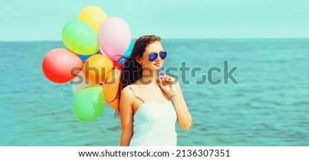 Summer image of happy young woman with colorful balloons on beach, sea background