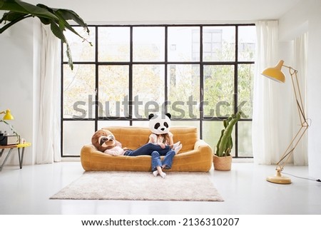 Two unrecognizable women with animal mask bear panda lying at sofa home - Beautiful living room indoors people disguised