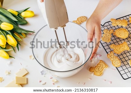 Cropped shot of woman using mixer machine making cookie icing for decoration. Woman holding glass bowl with sugar glaze and electric mixer. Easter holiday backing