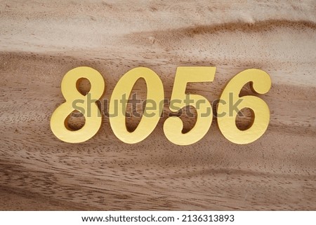 Wooden  numerals 8056 painted in gold on a dark brown and white patterned plank background.
