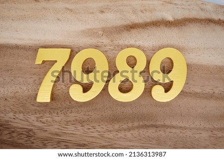 Wooden  numerals 7989 painted in gold on a dark brown and white patterned plank background.