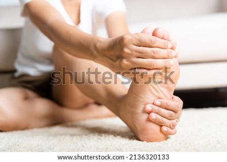Foot pain, Asian woman feeling pain in her foot at home, female suffering from feet ache use hand massage relax muscle from soles in home interior, Healthcare problems and podiatry medical concept Royalty-Free Stock Photo #2136320133