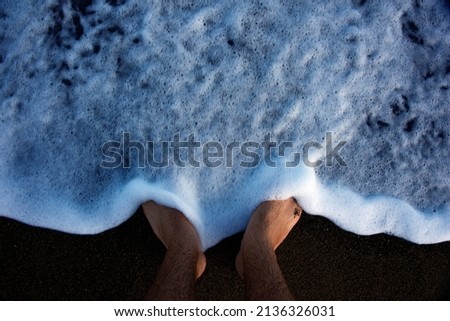 Wave foam water on man's feet with black sand background
