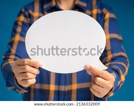 Hand holding of an empty white speech bubble against a blue background. A speech bubble concept. Space for text. Close-up photo