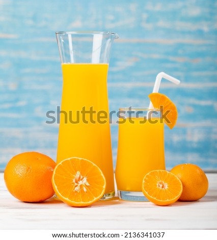 Fresh orange juice in jar and glass decorating with straw and fresh orange on white wooden table on blue wall. Studio picture concept for healthy diet