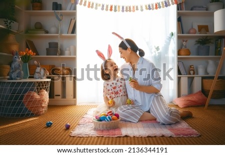 Happy holiday! Mother and her daughter with painting eggs. Family celebrating Easter. Cute little child girl is wearing bunny ears. 