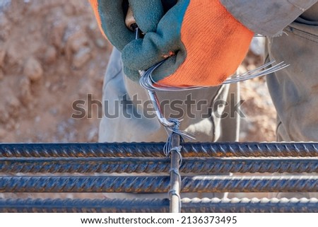 A worker uses steel tying wire to fasten steel rods to reinforcement bars. Close-up. Reinforced concrete structures - knitting of a metal reinforcing cage
