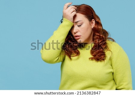 Young mistaken chubby overweight plus size big fat fit woman wear green sweater put hand on face facepalm epic fail mistaken omg gesture isolated on plain blue background. People lifestyle concept.