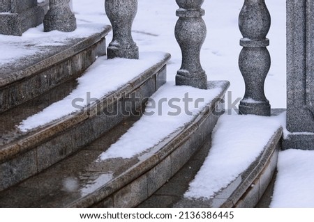 Balustrade of the rotunda under the snow. Gray granite exterior details during a snowfall. Fragment of a city landmark in winter. Selective focus. Blagoveshchensk, Russia.