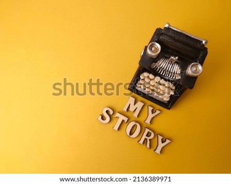 Selective focus.Wooden word and vintage black typewriter with text MY STORY on the yellow background.