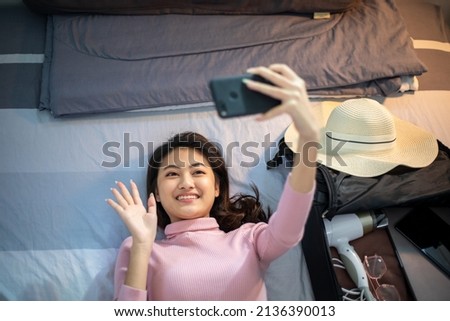 Beautiful Asian women using smartphone selfie and packing suitcases for travel
