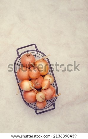 Fresh yellow onions in a metal basket on a light background. Top view. A copy of the space.