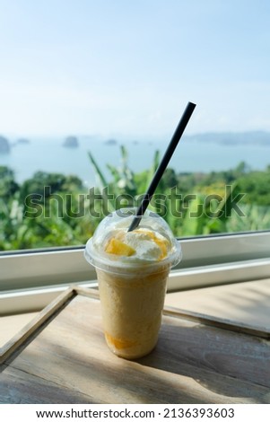 Mango smoothie put in glass on table Cafe sea island mountain background. Mango yogurt smoothie set up on wooden plate