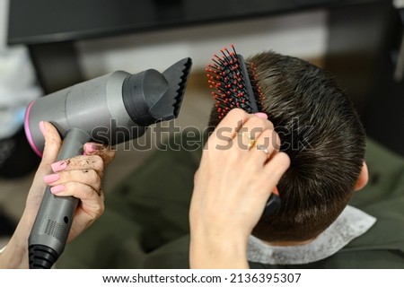 Teen guy gets a haircut during a pandemic in a barbershop, haircut and drying hair after a haircut, styling hair after a haircut with a hair dryer. Royalty-Free Stock Photo #2136395307